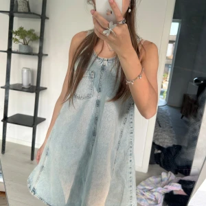Ljus jeansklänning med ficka - Säljer en ljusblå skitcool jeansklänning med rund halsringning och en bröstficka från Asos. Klänningen är ärmlös och har synliga sömmar som ger en cool och avslappnad look. Perfekt för varma sommardagar