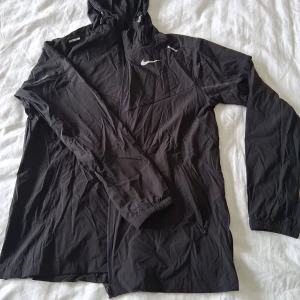 Svart vindjacka från Nike - Säljer en svart vindjacka från Nike med huva och dragkedja framtill. Säljs i nytt skick & billigt pris för den inte passar mig.