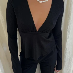 Nelly svart topp - Svart v-ringad topp i nelly-modell med ett band som du kan knyta fram eller bak, perfekt för både fest och vardaglig look. Använd ett par gånger, som ny.