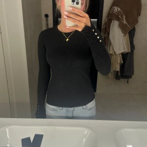 Mörkgrå/svart stickad tröja med guldknappar - Snygg mörkgrå/svart stickad tröja med lång ärm och guldknappar som detalj vid ärmslutet. Köpt från zara i storlek s