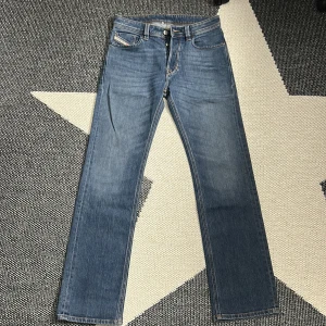Blå  jeans från Diesel - Säljer ett par klassiska blå jeans från Diesel med raka ben och snygga detaljer. Jeansen har fem fickor, knappgylf och coola sömmar på bakfickorna. Perfekt för dig som gillar tidlös stil och vill ha ett par jeans som funkar till allt.