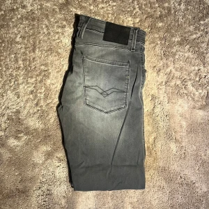 Replay anbass - Snygga grå jeans från Replay med klassisk femficksdesign och raka ben. Jeansen har diskreta slitningar och coola detaljer på bakfickorna. Passar dig som gillar en stilren look med lite edge. Materialet är mjukt och stretchigt jeans för extra komfort.