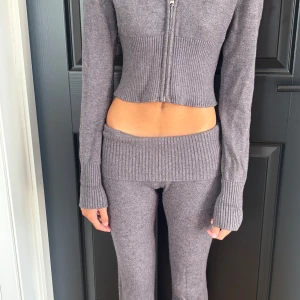 Grå ribbade mjukisbyxor Gina Tricot - Snygga grå mjukisbyxor från Gina Tricot med bred ribbad midja i låg modell. Byxorna är stickade i mjukt material och har en rak passform som ger en chill vibe. Perfekta för att hänga hemma eller när du vill vara extra comfy.