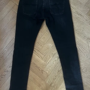 Slim/skinny nudie jeans - Säljer ett par svarta slimfit jeans från Nudie med modellen skinny lin. Jeansen har en klassisk femficksdesign och diskreta sömmar på bakfickorna. Jeansen har en slim/skinny passform och är tillverkade i stretchigt denim för extra komfort. Den ända deffekten är ett litet hål på inne fickan, men verkligen inget märkvärdigt. 