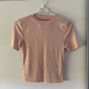 Ljusrosa ribbad topp från Gina Tricot - Supersöt ljusrosa ribbad topp från Gina Tricot med korta ärmar och rund hals. Perfekt basic att ha i garderoben, enkel att matcha med allt. Mjuk och stretchig bomullskvalitet som sitter skönt och har en slim passform.