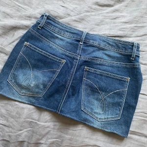 Vintage lowwaist jeanskjol - Säljer denna as snygga blå jeanskjol med coola och klassiska broderingar på bakfickorna från denim. Den har olika blå nyanser vilket är en så snygg detalj.