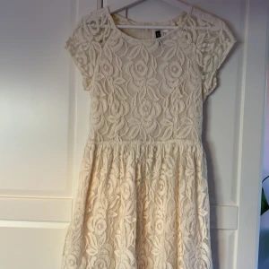 Vit spetsklänning från H&M Divided - Vit kortklänning från H&M Divided med blommigt spetsmönster och rund hals. Klänningen har korta ärmar och dragkedja i ryggen. 