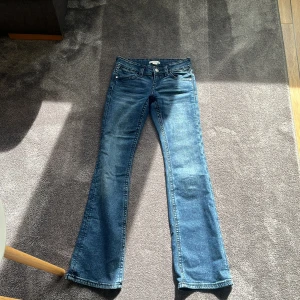 Blå bootcut jeans från Gina Tricot - Snygga blå jeans från Gina Tricot i bootcut-modell med klassisk femficksdesign och silverfärgade knappar. Jeansen har normal passform och är tillverkade i jeansmaterial med lätt tvättad look. Perfekta för dig som gillar retrovibbar och vill ha ett par jeans med lite utsvängda ben.