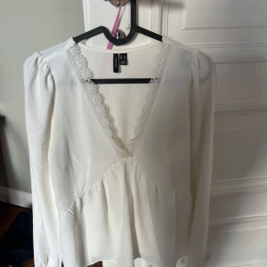Vit blus med spets från Vero Moda - Supersöt vit blus från Vero Moda i storlek XS. Blusen har långärmade puffärmar, v-ringad hals med spetskant och volang nedtill. Tillverkad i mjuk bomull. Den har en fläck på armen går bort i tvätten! 