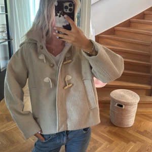 Beige ulljacka med träknappar - Säljer en beige jacka i ull med snygga träknappar och repdetaljer framtill. Jackan har en loose passform, två fickor och lång ärm. Perfekt för dig som gillar en chill och stilren look under höst och vinter. de är storlek 13-14 164cm med passar S jätte bra
