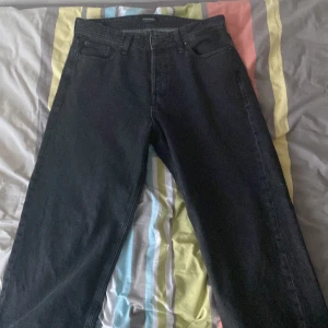 Svarta baggy jeans Jack & Jones - Säljer ett par svarta baggy jeans från Jack & Jones, modell Baggy/Alex. De har klassisk femficksdesign och bredare ben för en avslappnad vibe. Materialet är slitstarkt jeans och färgen är mörk svart, perfekt för dig som gillar streetwear och loose fit.