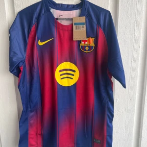 FC Barcelona Pedri matchtröja Nike - Säljer en officiell FC Barcelona matchtröja från Nike med Pedri och nummer 8 på ryggen. Tröjan har klassiska blå och röda vertikala ränder, gula detaljer och klubbmärke på bröstet. Kortärmad och tillverkad i lätt, ventilerande polyester. Perfekt för dig som älskar Barca och vill ha en snygg tröja med Spotify-logga.