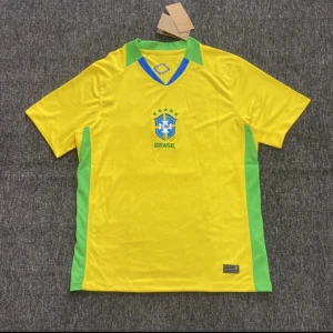Brasilien gul fotbollströja CBF - Gul Brasilien fotbollströja med gröna detaljer och CBF-emblem på bröstet. Tröjan har korta ärmar och V-ringad krage med blå inslag. Perfekt för dig som vill visa support för landslaget. Materialet är lätt och andas, idealiskt för match eller träning.