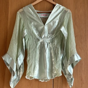 Mintgrön blus i silke från Holly Collection - Blus i silke med glittrigt tyg. Öppna, vida ärmar. Har viss tråddragning framtill samt saknar band som ska vara under bröstet. Jättefin passform och otroligt fint tyg. 