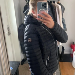 Marin blå dunjacka från Colmar med huva - Säljer en marinblå dunjacka från Colmar med snygg quiltad design och huva. Jackan har silverfärgade dragkedjor fram och vid fickorna, samt ett Colmar-märke på ärmen. Perfekt för kyliga dagar och har en clean look. Det är fransk storlek (liten i storlek) så det står att den är i storlek 48 men den passar som en S, jag är själv 170 och den sitter super bra. En söm som har gått upp lite men det syns inte och man kan även klippa bort den lilla tråden som syns. 