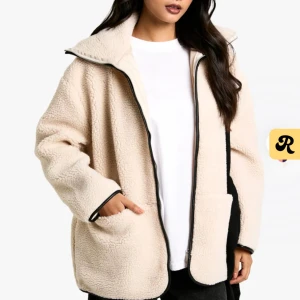Beige teddyjacka med dragkedja - Säljer en beige teddyjacka med oversized passform och långärmade ärmar. Jackan har en hög krage, två stora fickor framtill och svarta detaljer längs dragkedjan och ärmsluten. Materialet är mjuk fleece som ger en mysig vibe och passar perfekt för kyliga dagar. Väldigt stilren men bekväm och passar perfekt till hösten!