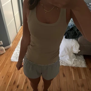 Beige ribbad linnetopp - Snygg beige linnetopp med ribbad struktur och rundad halsringning. Modellen är ärmlös och har en slim passform som sitter skönt mot kroppen. Perfekt att matcha med jeans eller shorts för en chill look. använd få gånger