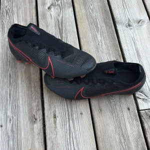 Nike Vapor 360 fotbollsskor svart/röd saknar skosnören - Säljer ett par Nike Vapor 360 fotbollsskor i svart med röda detaljer och sula. Skorna har en strömlinjeformad design med stickad ovandel och röda Nike-loggor längs sidorna. Perfekt för dig som vill ha grym kontroll och speed på planen.