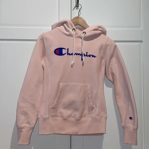Ljusrosa Champion hoodie med logga, storlek xs - Säljer en figursydd ljusrosa hoodie från märket Champion, storlek xs men är som xxs. Hoodien har en stor logga på bröstet och en liten logga på armen. bra skick och är använd ca 4 gånger. priset kan diskuteras.