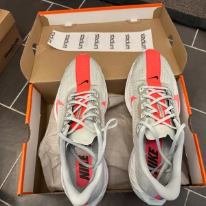 Nike zoomx Pegasus turbo plus vit/rosa - Nike ZoomX  pegasus turbo plus sneakers i ljusgrått med starkt rosa detaljer och swoosh. Ovandelen är ventilerande mesh, snörning och platt sula med svart och rosa grepp. Perfekt för dig som vill maxa din löpning med stil och komfort.