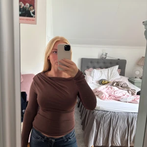 Brun offshoulder topp med omlott - Säljer en brun långärmad topp med snygg omlott-detalj och offshoulder-design. Toppen har en tight passform som framhäver figuren och är perfekt för dig som gillar trendiga och stilrena plagg. Materialet känns mjukt och stretchigt mot huden.