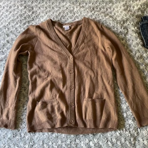 Beige kofta från Anne Weyburn - Säljer en beige/brun kofta från Anne Weyburn med v-ringning och knappar framtill. Koftan har två fickor fram och ribbade muddar vid ärmslut och nederkant. Kolla gärna mina andra annonser!