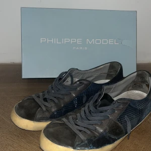 Philippe Model blå sneakers - Snygga sneakers från Philippe Model i mörkblått med coolt rutigt mönster på sidorna. Skorna är i dåligt skick, varav mycket lågt pris. Om de lämnas in på reparation för ca 900kr kan de bli nära nyskick igen skulle jag tro! Kom DMs vid minsta fundering 🤔🙌| största defekt är trasiga sulor |storlek 45 låda medföljer