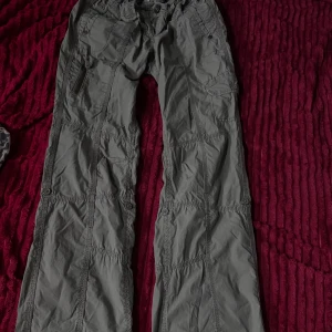 Gröna cargopants med fickor by S. OLIVER.  - Säljer ett par gröna cargopants by S. OLIVER  med flera fickor och coola sömdetaljer. Byxorna har låg midja och knappar på bakfickorna. Materialet är syntet och ger en avslappnad loose passform. Perfekt för dig som gillar streetstyle och praktiska detaljer.