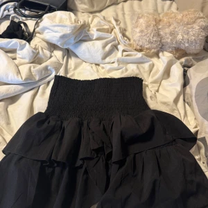 Svart volangkjol från Neo Noir - Supersnygg svart kjol från Neo Noir med bred smock i midjan och dubbla volanger som ger en cool och feminin vibe. Kjolen är gjord i mjuk polyester och har en kort passform som är perfekt för att styla med crop tops eller hoodies.