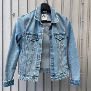 Ljusblå jeansjacka från Zara - Snygg ljusblå jeansjacka från Zara med klassisk krage, knappar framtill och två bröstfickor med lock. Jackan har slitna detaljer vid krage och ärmslut! Jackan är i ett jätte fint skick, om du har några fler frågor är de bara att skriva🫶