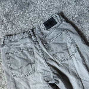 Grå Jack&Jones Jeans   - Snygga grå jeans från Jack & Jones med klassisk femficksdesign och raka ben. Storlek 176. Jeansen har en cool tvättad look och detaljerade sömmar på bakfickorna. Passar dig som gillar en avslappnad stil med lite edge.