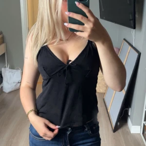 Svart linnetopp med knyt framtill - Snygg svart linnetopp med v-ringning och knyt framtill. Toppen är ärmlös och har tunna axelband!💞stl s/m