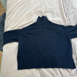 Svart polotröja med ribbad krage - Svart polotröja i storlek S med hög, ribbad krage och breda ribbade muddar vid ärmslut och nederkant. Tröjan har lång ärm och är stickad i ett mjukt material, perfekt för kyliga dagar. Enkel och stilren design som funkar till många olika outfitsanvänd max 2 gånger.