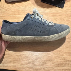 Saint Laurent Skor - Snygga Blå sneakers från Saint Laurent i mjuk mocka med handskriven logga på sidan och präglad logga på hälen. Skon har vit platt sula och vita snören som ger en clean vibe. Perfekt för dig som gillar stilrena och exklusiva sneakers.