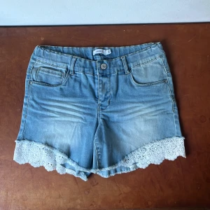 Ljusblåa/blåa jeansshorts med spetsdetalj - Säljer nu dessa fina jeansshorts med spetsdetaljer från Name It! Köpt på Karlaplan loppis och har själv inte använt dem sedan dess, men jag skulle placera varan som mycket bra skick! 🩷😇