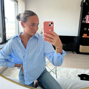 Blå randig skjorta med klassisk krage - Snygg blå skjorta med vita ränder och klassisk krage. Skjortan har lång ärm och knappar framtill. Perfekt att styla med jeans för en chill och fräsch look. Materialet känns lätt och bekvämt mot huden.