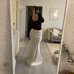 Lång champagnefärgad satinkjol från Musera - Supersnygg långkjol i champagnefärgad satin. Kjolen har en slät, figurnära passform med lätt utsvängd nederdel och midjehöjd. Materialet är glansigt och mjukt, perfekt för att ge en lyxig vibe till din outfit. Prislappen är kvar.