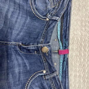 Blå lowwaist bootcut jeans med detaljer - Säljer ett par blå jeans med bootcut passform och låg midja. Jeansen har snygga kontrastsömmar, dekorativa knappar och coola bakfickor( lånade bilder)