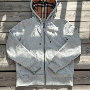 Grå Burberry hoodie med rutig huva - Säljer denna riktigt feta Burberry med deras vanliga rutiga foder på insida och huva, Tröjan är i toppskick 10/10! Storlek S men är lite stor i passformen så S-M. Ved mer frågor hör gärna av er! Mvh🏌️