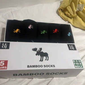 Svarta bambustrumpor med älgmotiv - Fem par svarta bambustrumpor från LEOJ med broderade älgar i olika färger: gul, rosa, grön, röd och blå. Strumporna är mjuka och andas bra tack vare bambumaterialet. Perfekt för dig som gillar lite färg och vill ha något unikt på fötterna.