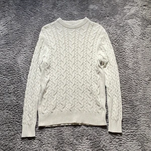 Vit kabelstickad tröja från 157 - Säljer en vit kabelstickad tröja från 157 i storlek M. Tröjan har ett klassiskt flätmönster, rund hals och ribbade muddar vid ärmslut och nederkant. Perfekt för dig som gillar stilrena och mysiga plagg med lite preppy känsla.