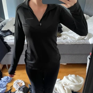 Svart långärmad träningströja Craft - Svart långärmad träningströja från Craft med halv dragkedja framtill. Slim passform som sitter snyggt mot kroppen och funkar perfekt till gymmet eller löprundan. Materialet är mjukt och följsamt, och tröjan har en stilren look med diskret logga på bröstet.