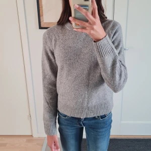 Grå stickad tröja från H&M - Mysig grå stickad tröja från H&M med rund hals och ribbade muddar vid ärmslut och nederkant. Perfekt för kyliga dagar och enkel att matcha med jeans eller kjol. Klassisk modell med lång ärm och mjukt material som känns skönt mot huden. Denna tröja är bara använd ett fåtal gånger.