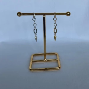 Asymmetriska örhängen i silver och guld - Snygga asymmetriska örhängen med hängande detaljer i både silver och guld. Ena örhänget har en silverfärgad kedjelänk och konformad spets, medan det andra har samma design i guld. Båda har små ringar och en glittrig yta på själva ringen. Perfekt för dig som gillar unika smycken.