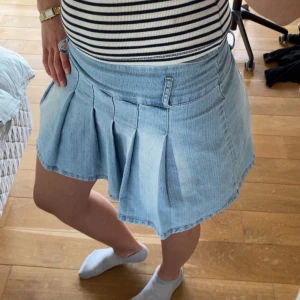 Ljusblå jeanskjol med volang vek - Säljer en ljusblå jeanskjol med bred linning och markerade veck. Kjolen har hällor för bälte och är i en kort modell. Perfekt för dig som gillar en avslappnad och trendig stil. Står stolen L men skulle mer säga en M/s. Jag har sytt igenom där man knäpper den för tyckte inte det behövdes eftersom att den är lite stretchig.  