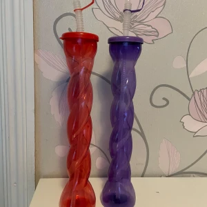 Röd och lila spiralformad plastflaska med sugrör - Två spiralformade flaskor i plast, en röd och en lila, med tillhörande lock och sugrör. Perfekt för dryck på språng eller till festliga tillfällen. Flaskorna har en twistad design som gör dem extra roliga att använda.