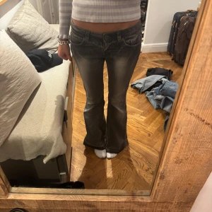 Lågmidjade bootcut jeans i mörkgrå tvätt - Säljer ett par lågmidjade bootcut jeans i mörkgrå tvätt med slitningar och klassiska fickor bak och fram. Jeansen har en lätt utsvängd passform nertill och är perfekta för en avslappnad och trendig look.