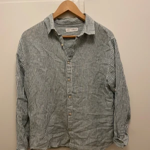 Randig linneskjorta från Zara - Säljer en snygg randig skjorta från Zara i vitt och grönt. Skjortan är tillverkad i linne och har långa ärmar samt klassisk krage och knäppning framtill. Perfekt för en avslappnad och stilren look.