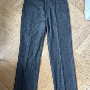 Oanvända breda grå kostymbyxor från Tiger of Sweden -  grå breda oanvända kostymbyxor från Tiger of Sweden med klassisk rak passform. Byxorna har diskreta fickor bak och fram samt stängs med knapp och dragkedja. Perfekta för en stilren look. Storlek 50. Förstora för mig. 100%bomull