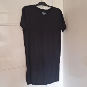 Svart t-shirt klänning från Newbody - En klassisk svart t-shirt från Newbody i 100% ekologisk bomull. Klänningen har rund halsringning och korta ärmar, perfekt för en enkel och stilren look. Passar dig som gillar basic och bekväma plagg. Funkar även som stilrent nattlinne!